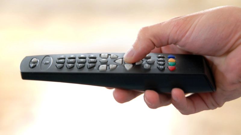 A man is pressing the keypad of the remote control.